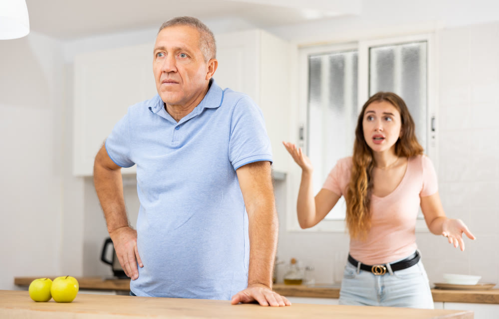 Adult daughter scolds an elderly father while he is preparing dinner in kitchen