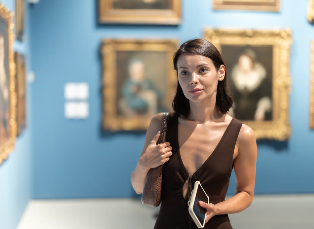 Woman with phone in hands in museum hall, view painting exhibition