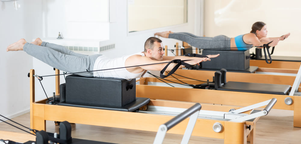 Atletic man doing pilates exercises with reformer bed in studio. Active lifestyle and fitness concept