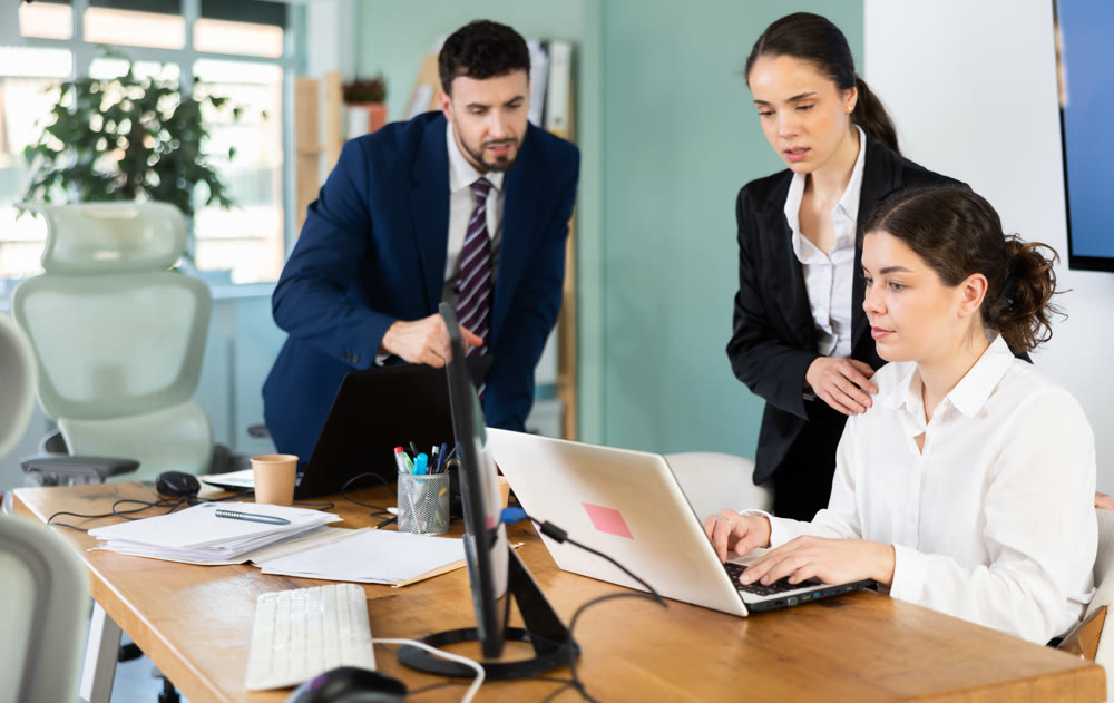 Man and woman help female colleague work with laptop