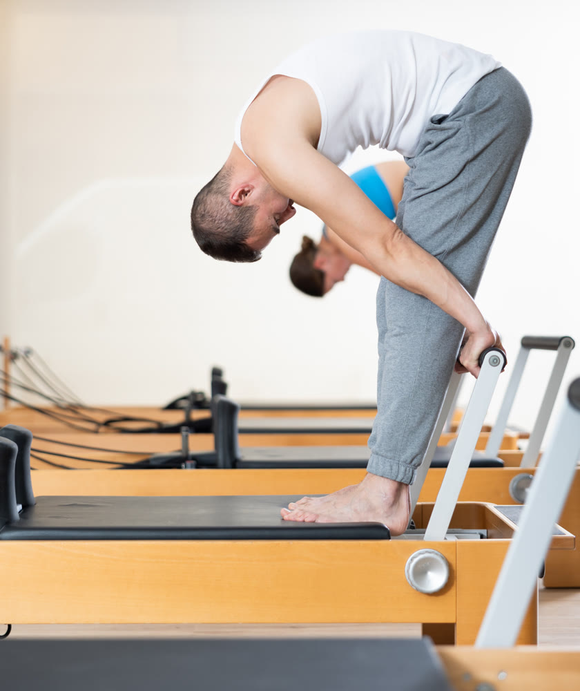 Man doing stretching exercises on Pilates reformer in fitness center