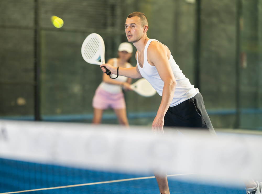 Young man and adult woman playing doubles tennis