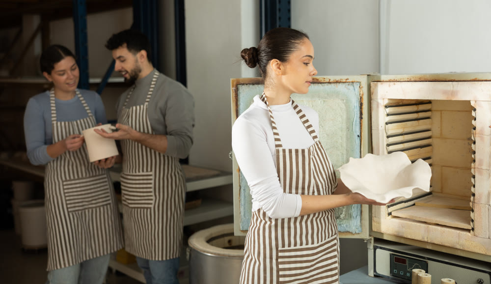Girl in apron put or takes clay vase out of oven