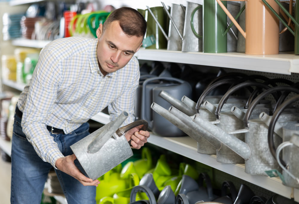 Young man choosing watering pot in hardware store
