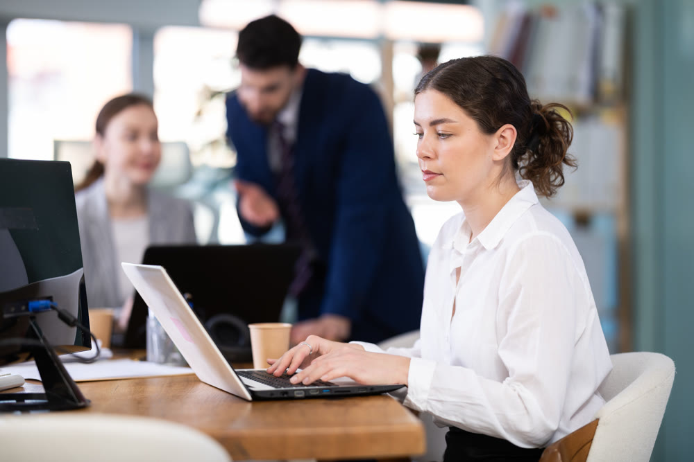 Young woman works on laptop with colleagues