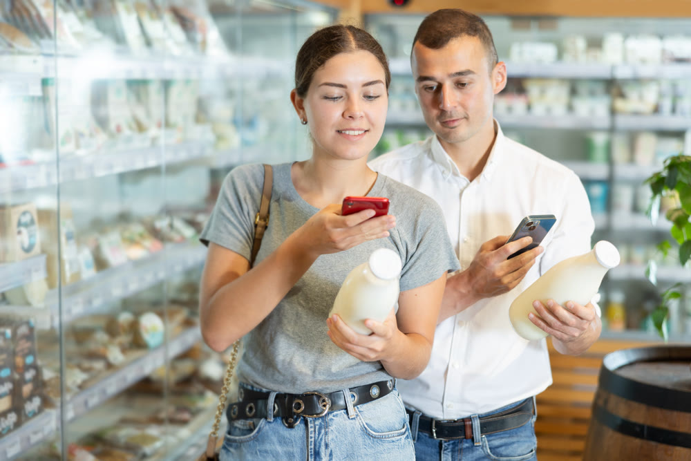 Positive young couple scanning QR code on milk bottle in large supermarket