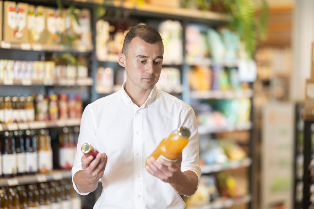 Interested man pondering choices of organic juices in natural food store