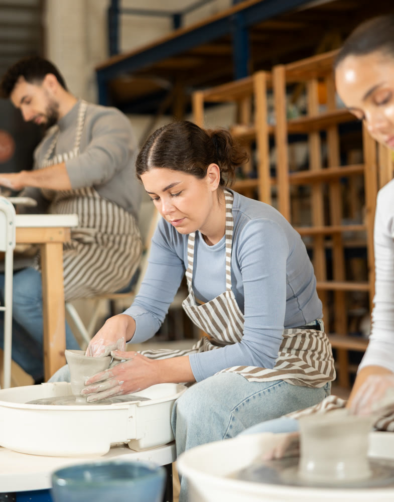 Two girls craftspersons busy molding clay products on pottery wheel