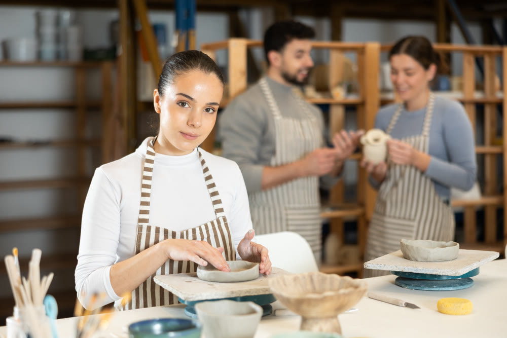 Girl sitting at table, busy making products from raw clay