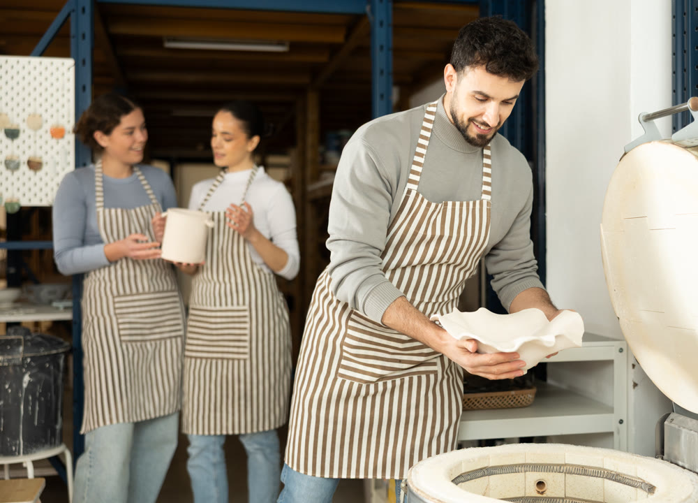 Man in apron put or takes clay vase out of oven