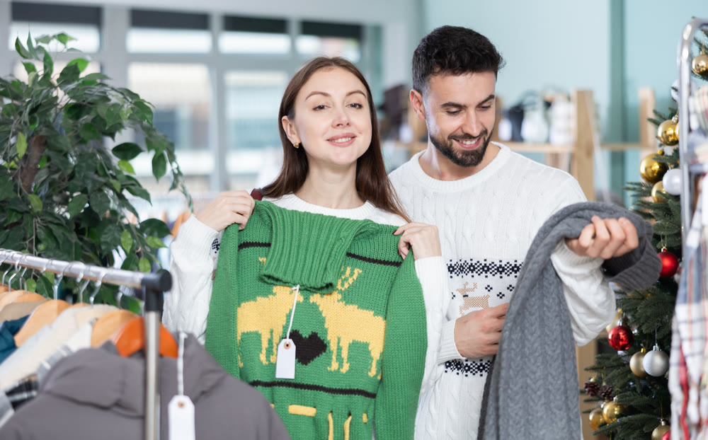 Couple choosing a warm sweater against the background of a Christmas tree in a decorated store