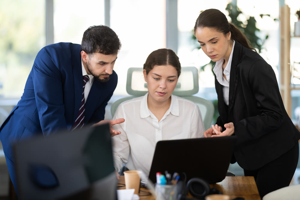 Group of colleagues discussing work around laptop in office