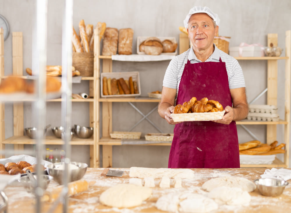 Smiling older baker presenting fluffy croissants in bakery