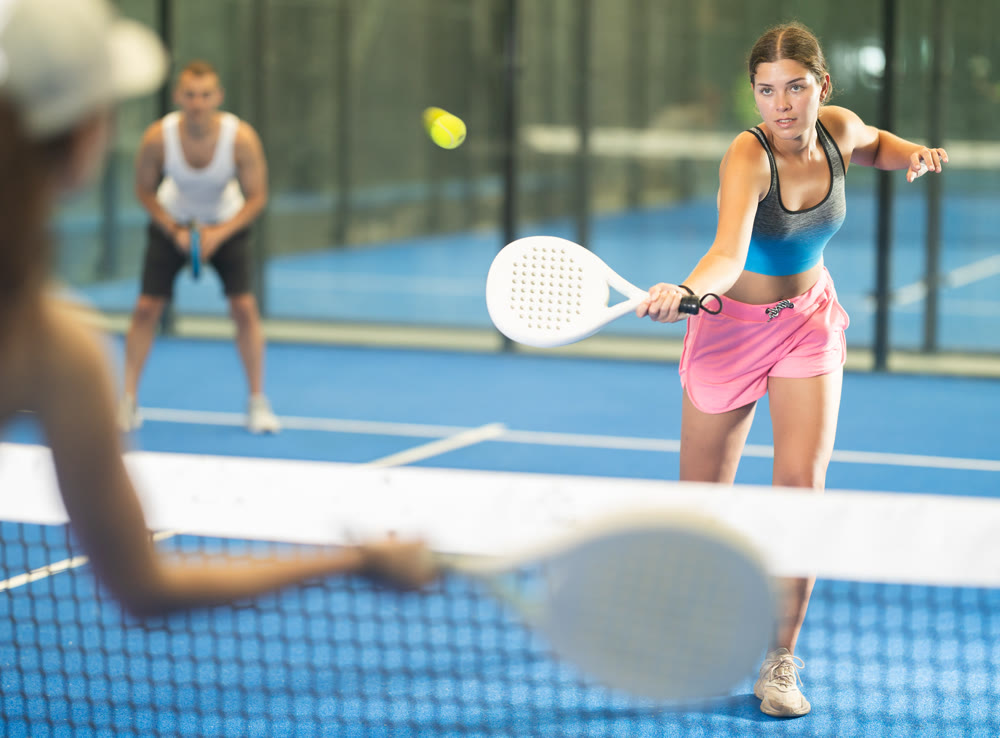 Girl paired with a man plays padel on an indoor tennis court