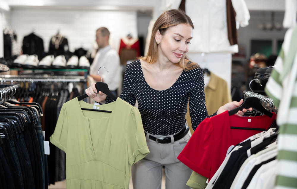 Young woman choosing dress in clothing store