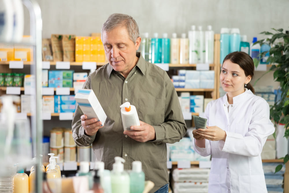 Female pharmacist helps mature man choose skin cream