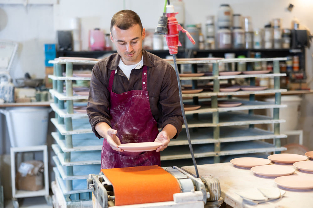 Young man polishing blanks of ceramic products