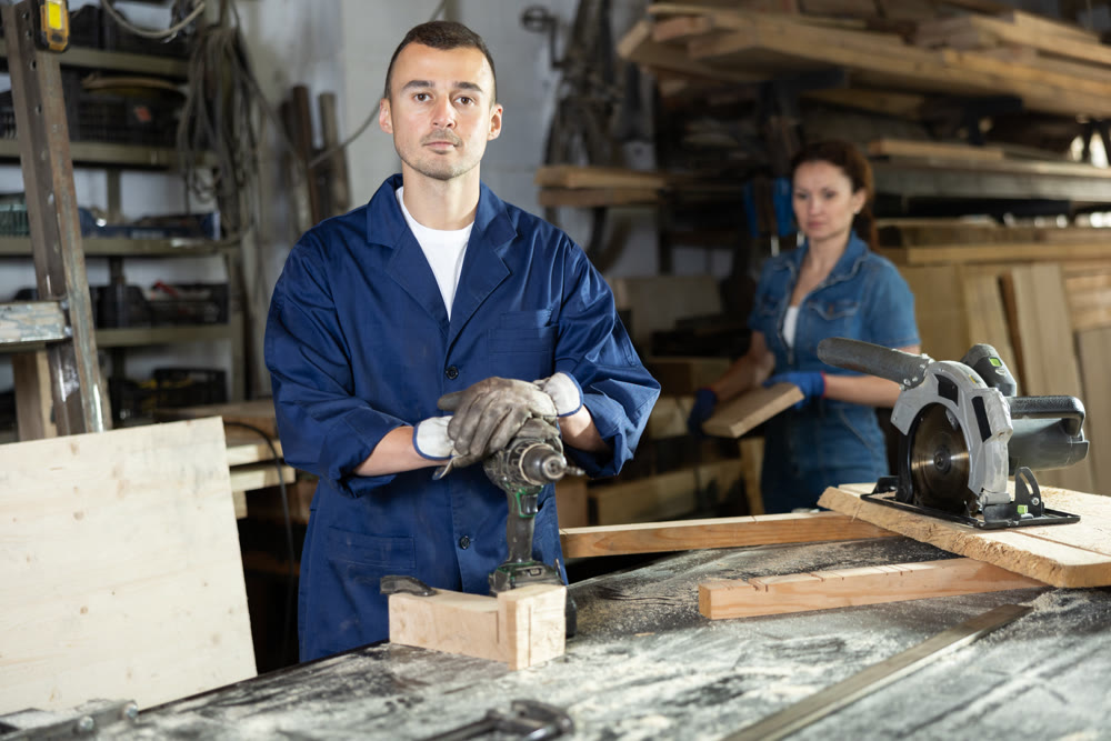 Male employee of carpentry workshop uses drill to make holes in wooden billet