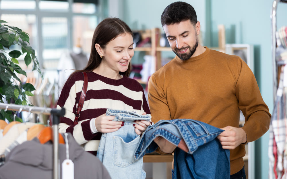 Woman selects jeans in clothing store. Man helps her