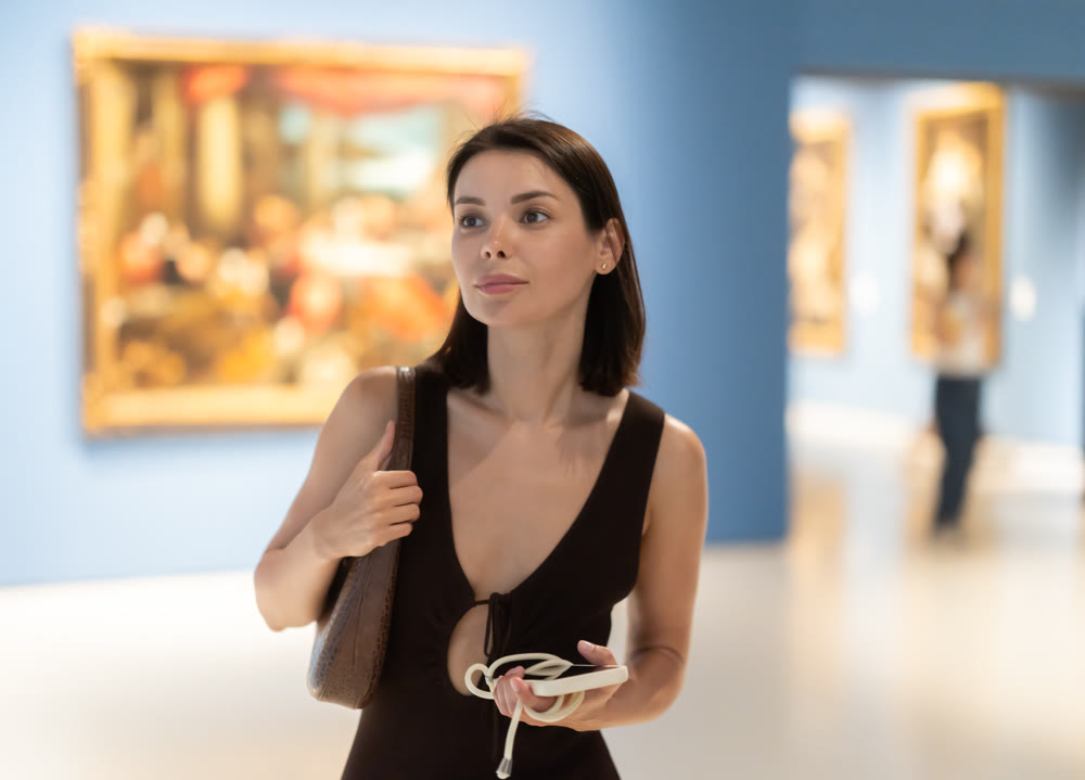 Woman visiting museum and looking at paintings in gold frames