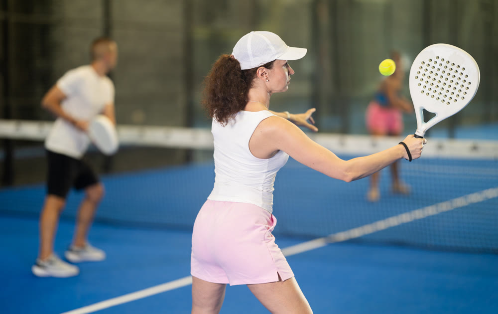 Woman in shorts jumping while playing padel tennis on court. Racket sport training outdoors