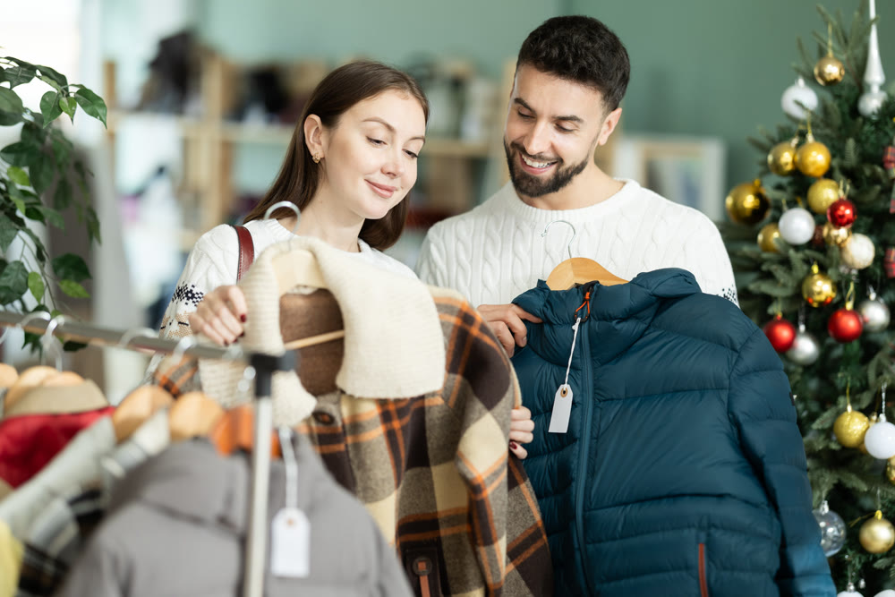 Focused woman looking coat for winter season and male salesperson or husband helping with assortment and choice in clothing store