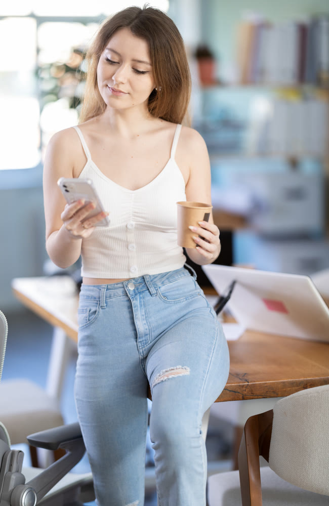 Young woman drinking coffee and scrolling through the feed on smartphone