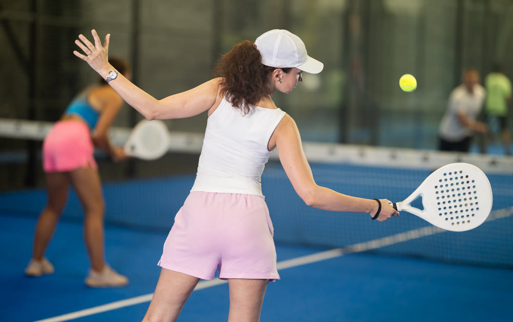 Woman with racket training on outdoor court playing padel game and hitting ball