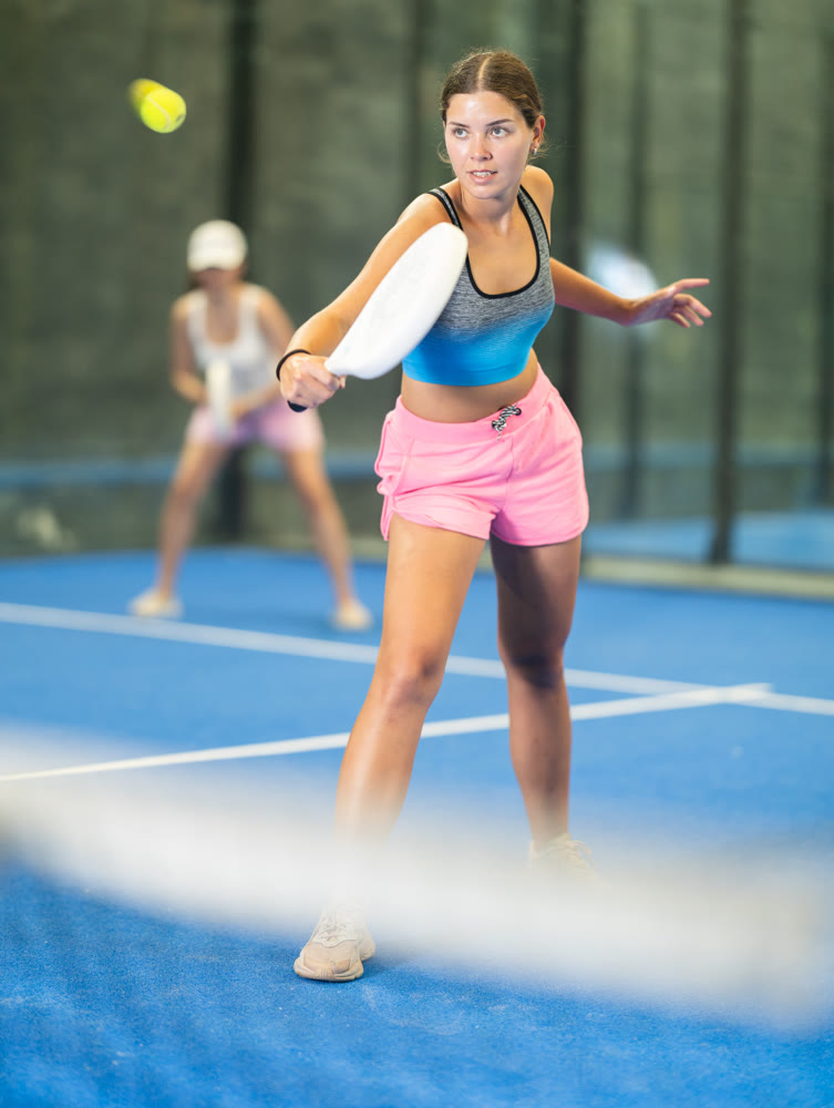 Sportive woman and other members engaged in Padel Tennis in indoor court of tennis club