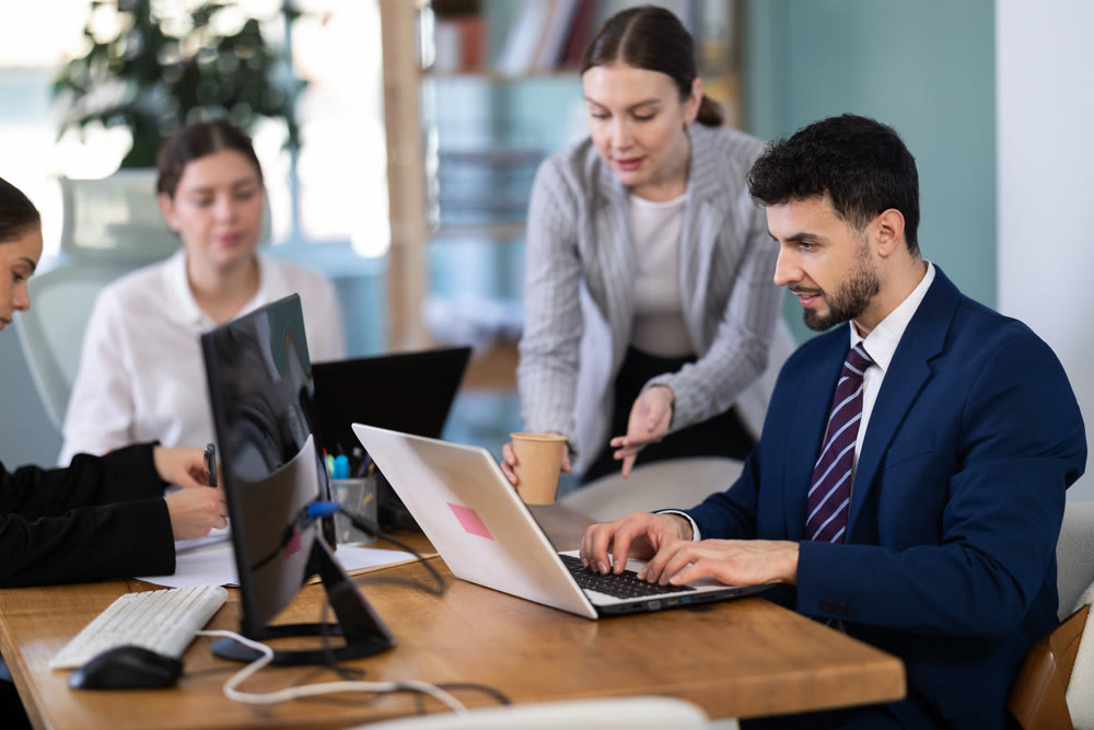 Young woman helping male colleague work on laptop