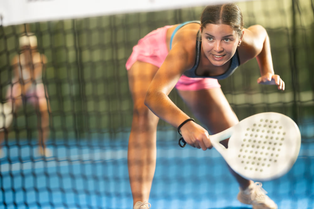 Female player playing padel in a padel court indoor behind net