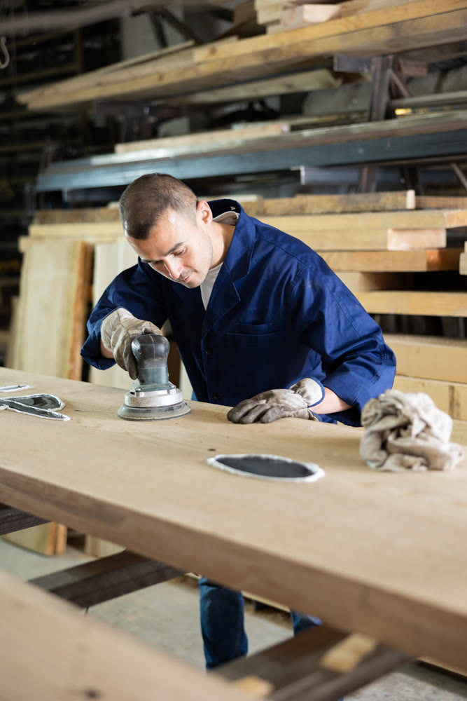 During manufacturing, man employee grinds surface of wooden board, gives smoothness to surface