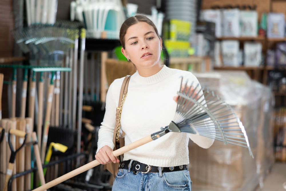 Girl carefully chooses rake in hardware store to clean garden
