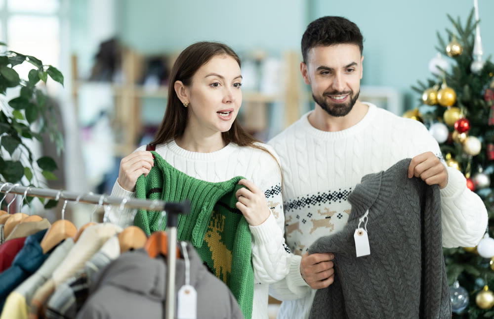 Married couple choose sweaters against background of Christmas tree in clothing store