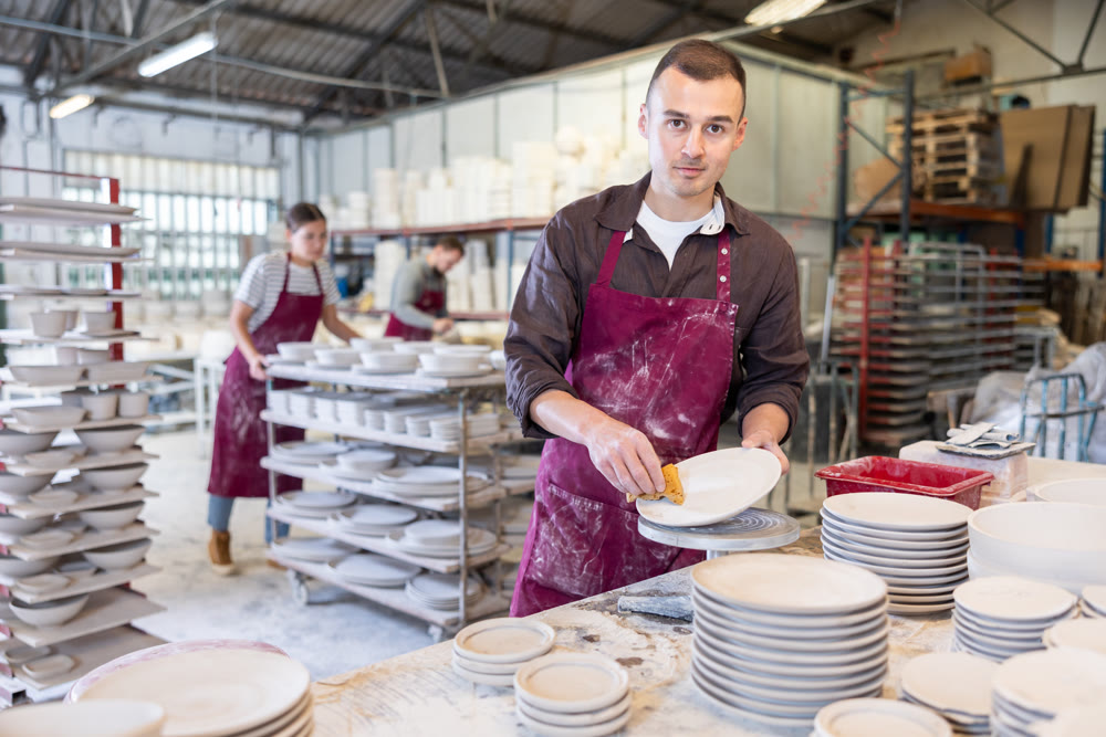 Skilled artisan cleaning plates with sponge in ceramics studio