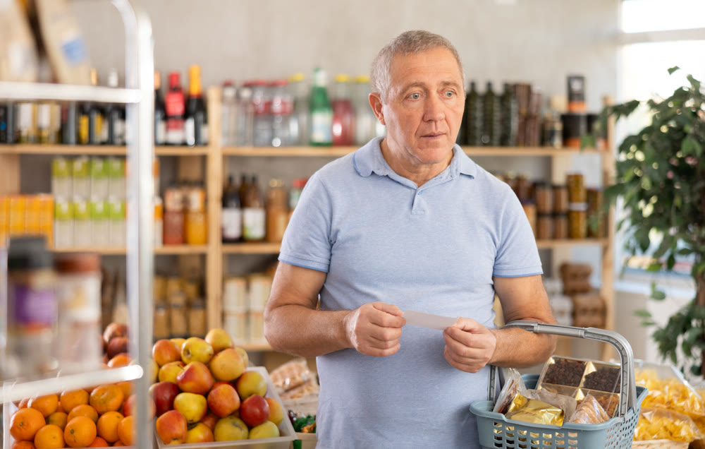 Elderly man buying groceries from shopping list in store