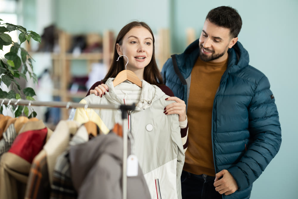 Happy couple examine and selecting clothes for cold season in modern store, man trying new coat
