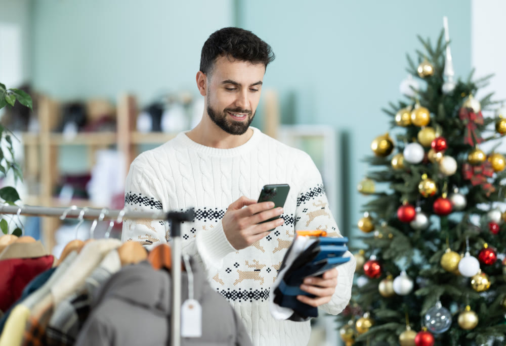 Man stands against the background of a Christmas tree and scans the barcode of socks packaging