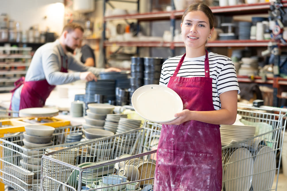 Smiling female artisan showcasing collection of ceramic plates in workshop