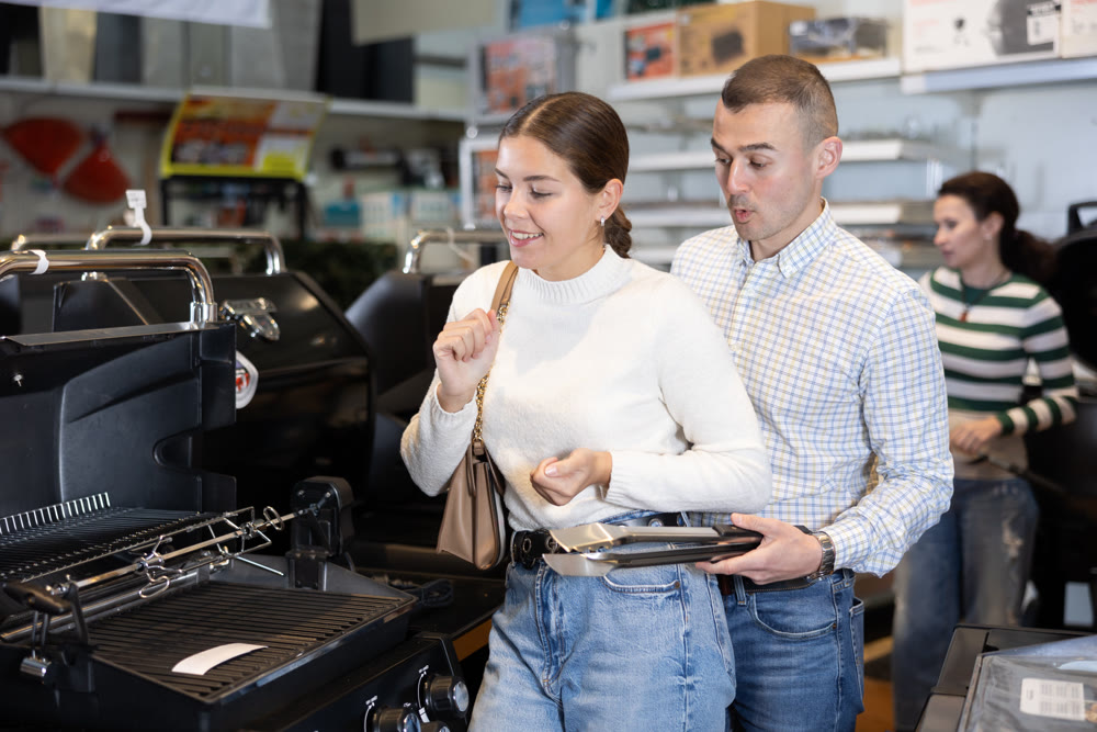 Young married couple chooses a new grill in supermarket for their yard