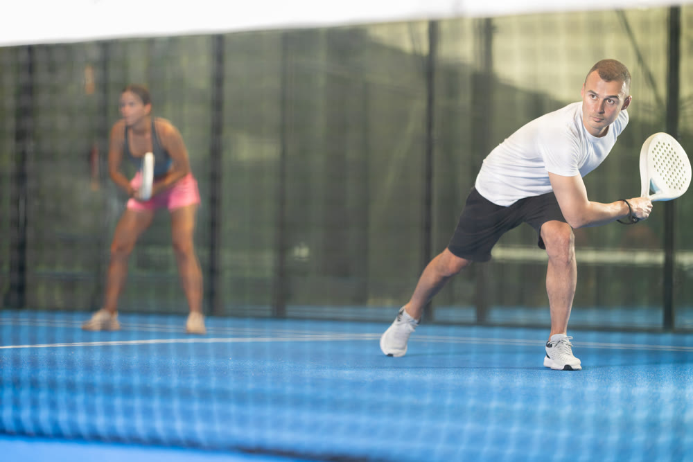 Male players playing padel in a padel court indoor behind net