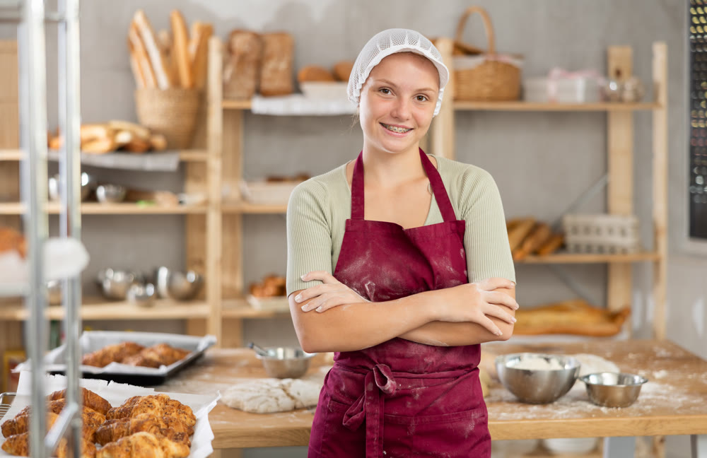 Enthusiastic young female baker standing with crossed arms in bakery