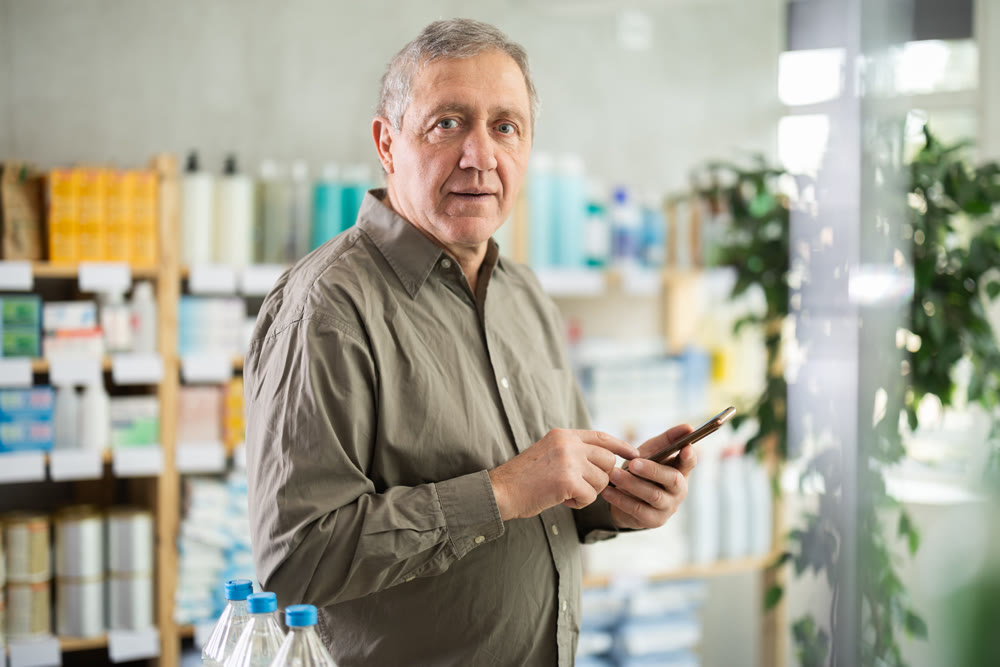 Mature man using mobile medical app to check prescription at pharmacy