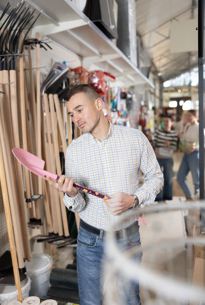Young man choosing shovel in store