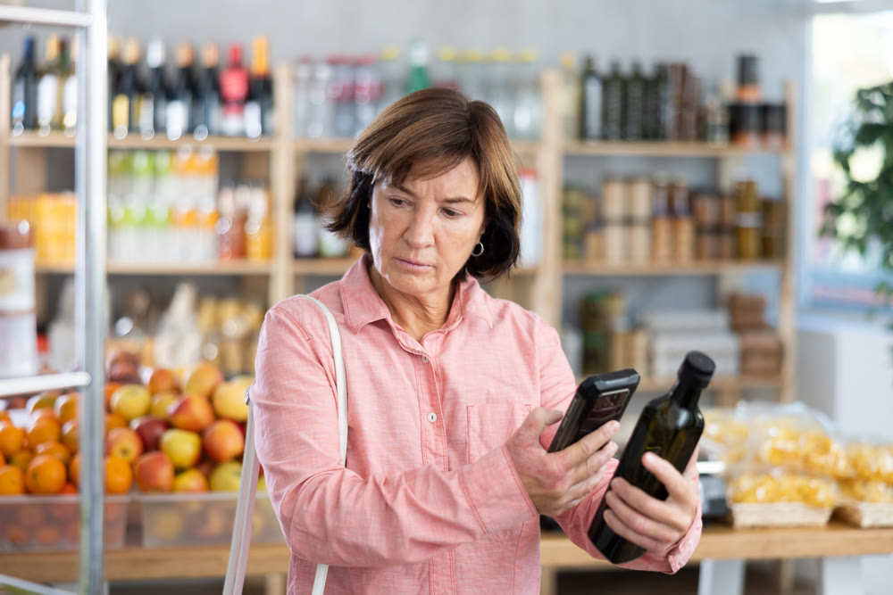 Mature woman is scanning QR on a bottle of olive oil in grocery