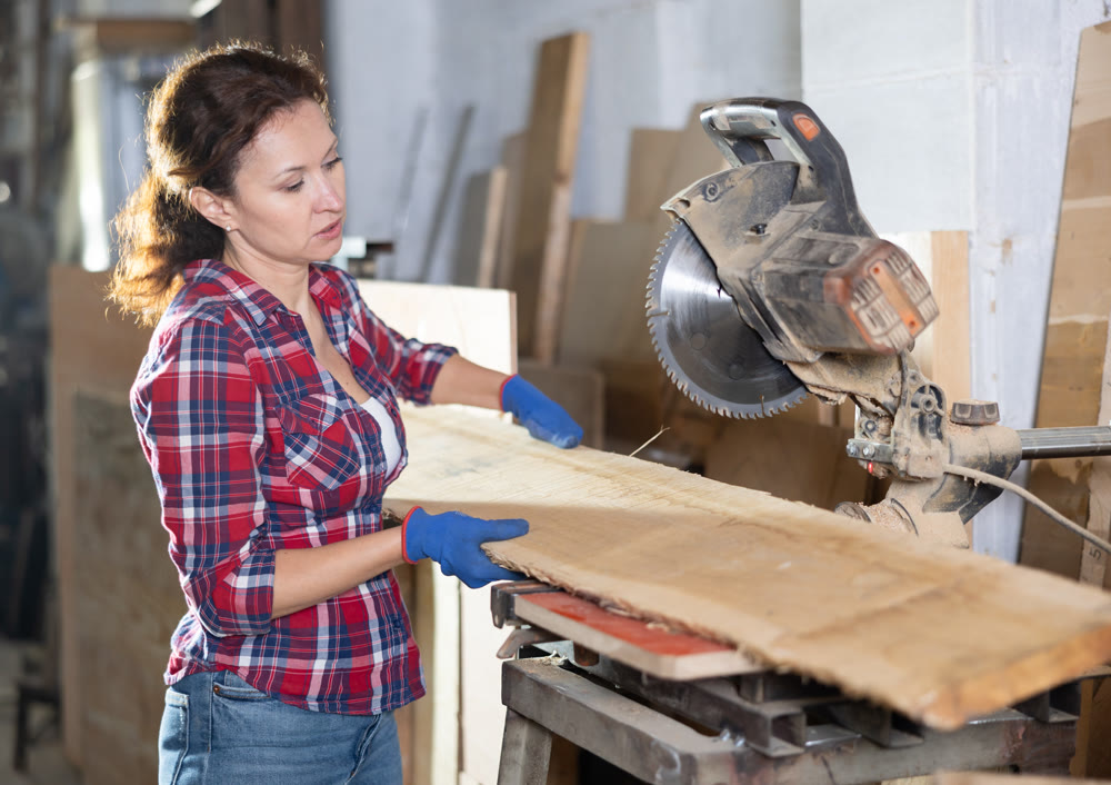 Working at sawmill - woman saws wooden board using circular saw