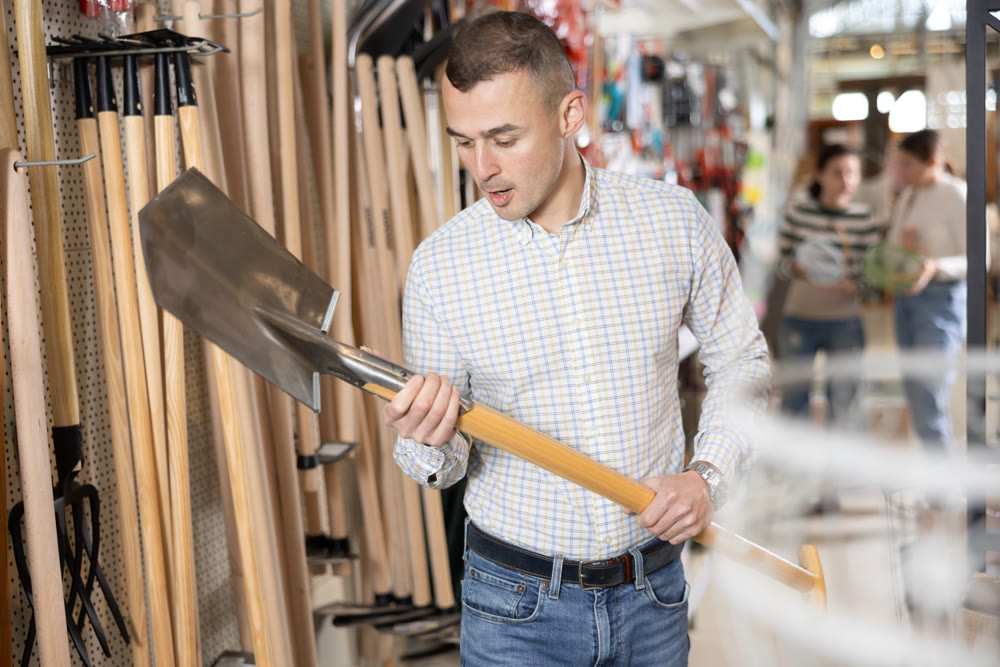 Buying shovel in supermarket - man with interest chooses shovel in hardware store for working in garden