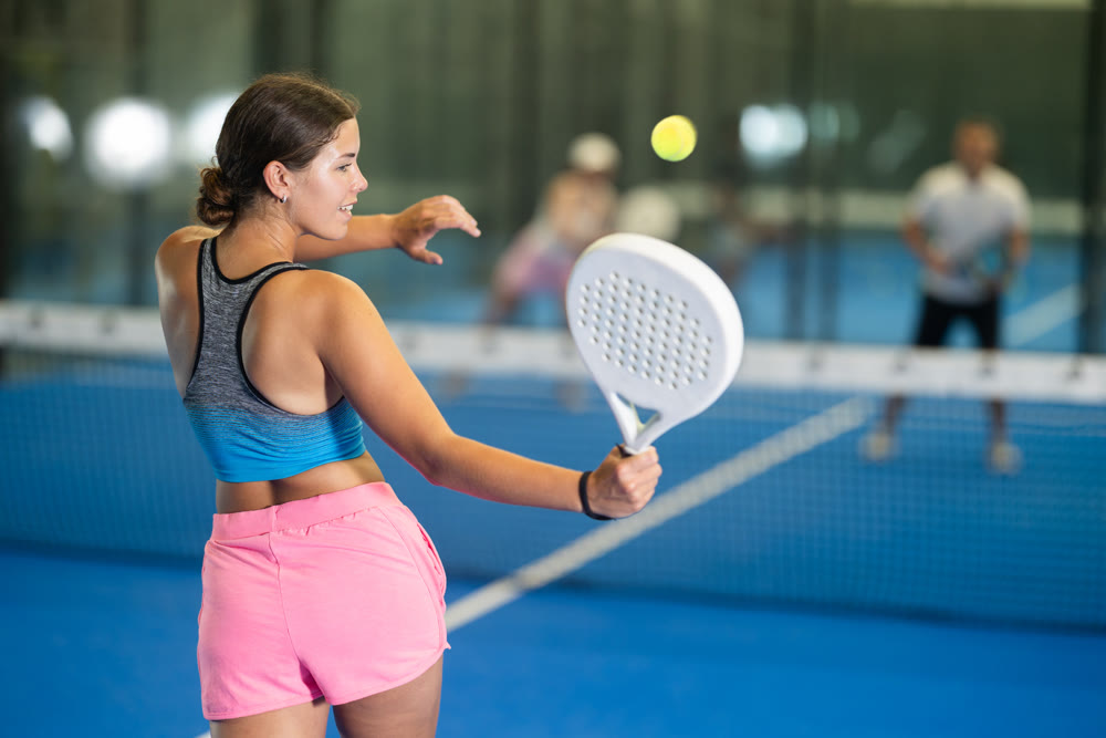 Young woman playing tennis against man and woman