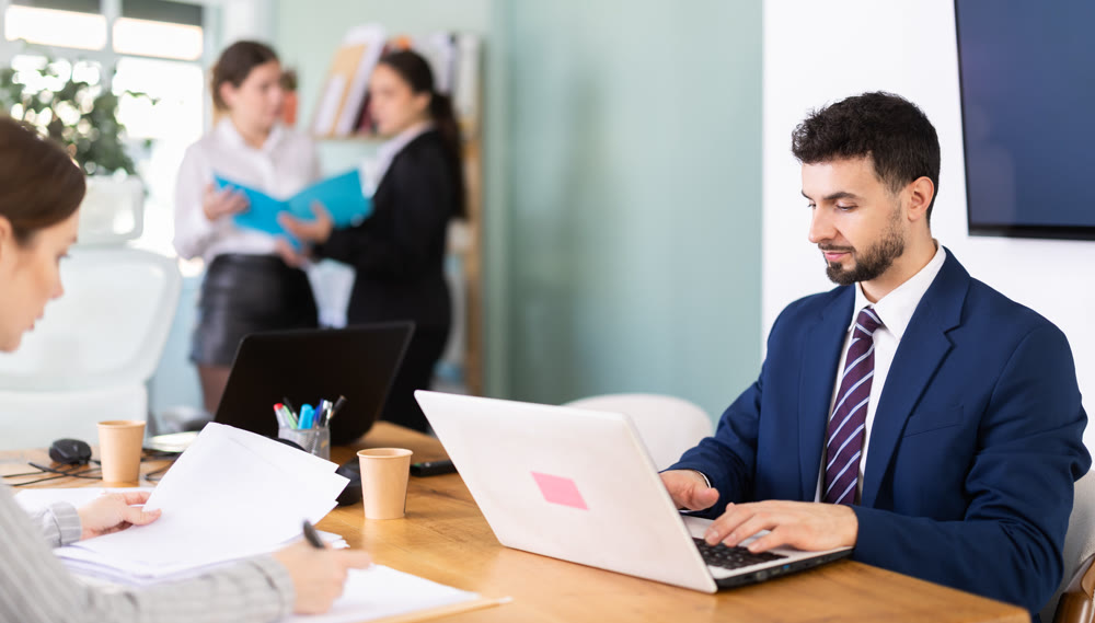 Man in a jacket sits at a table and works attentively on a laptop