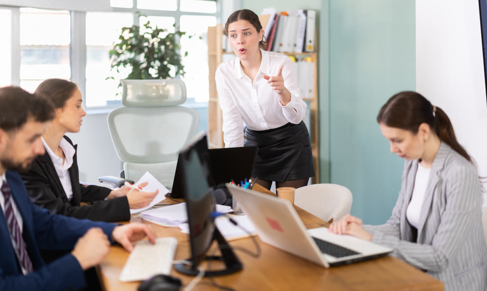 Young female manager standing and scolding colleagues during stressful corporate meeting